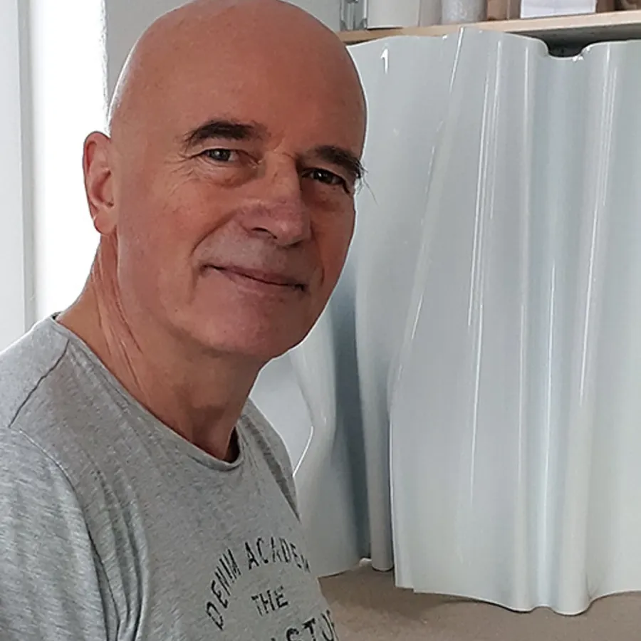 Bildhauer Kuno Vollet in seinem Atelier neben einer weißen, wellenförmigen Skulptur
