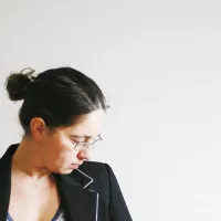 Bildhauerin Susanne Kraißer im Profil mit Brille und dunklem Blazer vor heller Wand