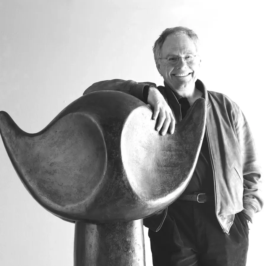 Bildhauer Werner Pfändler lächelnd mit der Hand auf einer großen geschwungenen Skulptur, Schwarz-Weiß-Aufnahme