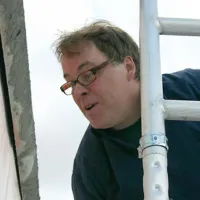 Bildhauer Pierre-Paul Maillé mit Brille bei der Arbeit auf einem Gerüst