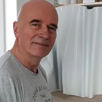 Bildhauer Kuno Vollet in seinem Atelier neben einer weißen, wellenförmigen Skulptur