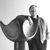 Bildhauer Werner Pfändler lächelnd mit der Hand auf einer großen geschwungenen Skulptur, Schwarz-Weiß-Aufnahme