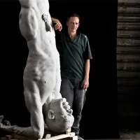 Bildhauer Tilmann Krumrey neben einer überlebensgroßen weißen Figur, die auf dem Kopf steht